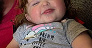 Chloe is registered to the contest to win money with this photo: toddler, child, smiling, happy, face, person, couch, clothing, gray_shirt, text_on_shirt, arm, hair, indoor, cozy, adult, holding, red_shirt, plush, relaxed, home