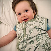 Amara joined the competition — help win amazing prizes! baby, child, infant, smiling, happy, face, portrait, blue_eyes, brown_hair, lying_down, pillow, bed, blanket, sleepwear, leaf_pattern, floral_pattern, indoor, close_up, candid, cozy