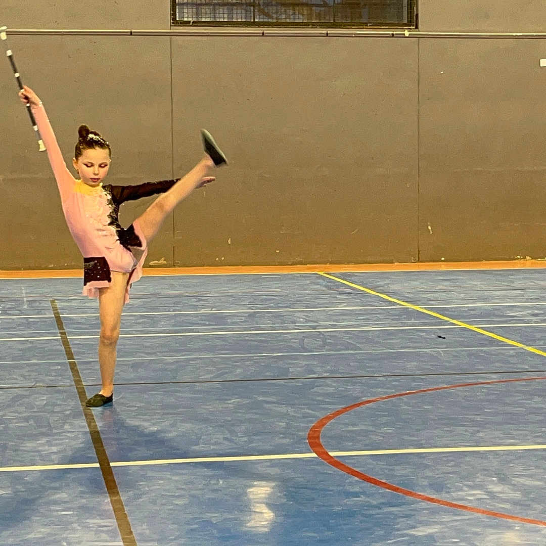 Ennélya a rejoint le concours — aidez-le/la à gagner de superbes lots ! athlete, balance, baton, black_outfit, blue_floor, child, concentration, dance, floor_markings, girl, gymnasium, gymnastics, indoor, performance, pink_outfit, pose, rhythmic_gymnastics, sport, sports_court, young