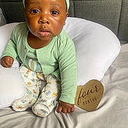 Nazir joined the competition — help win amazing prizes! baby, infant, child, pajamas, green_clothing, headwear, cushion, bed, white_bedding, wooden_sign, heart_shaped, four_months, portrait, indoor, cute, skin, face, eyes, hand, sitting