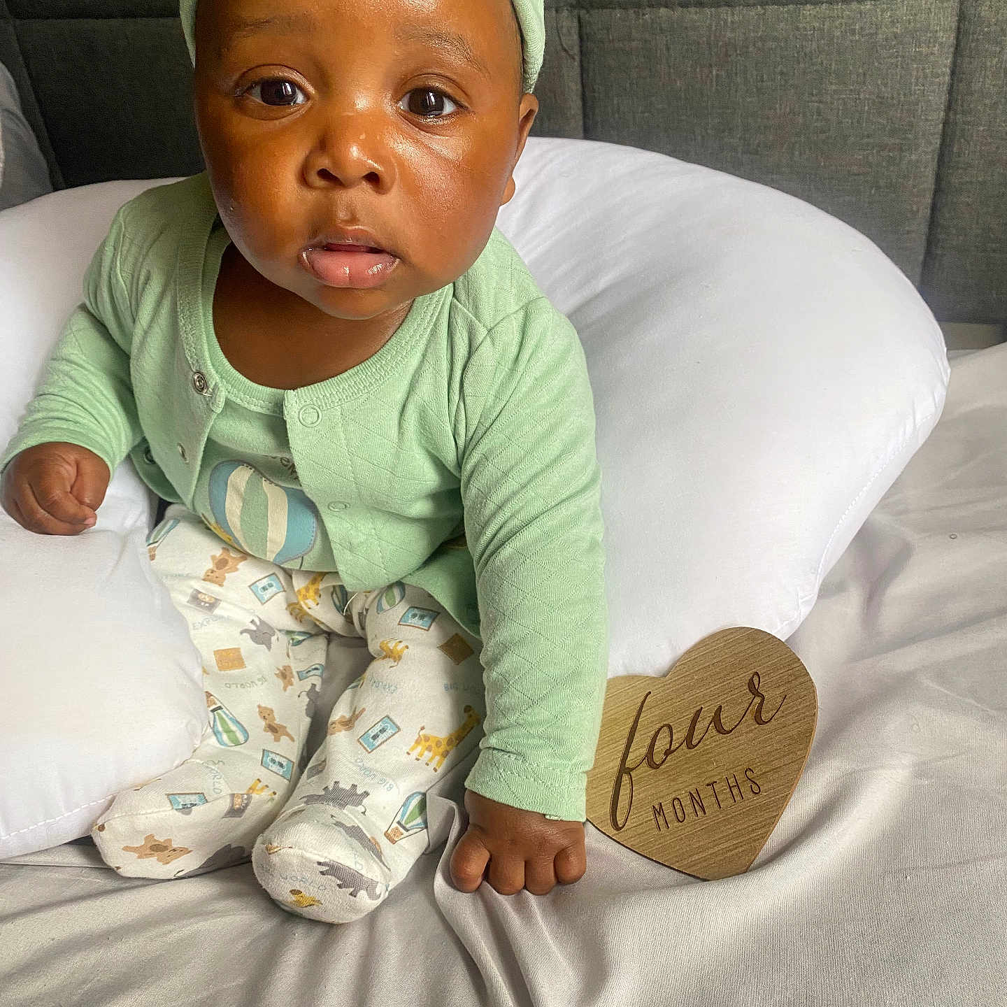Nazir joined the competition — help win amazing prizes! baby, bed, child, cushion, cute, eyes, face, four_months, green_clothing, hand, headwear, heart_shaped, indoor, infant, pajamas, portrait, sitting, skin, white_bedding, wooden_sign