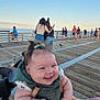 baby, smiling, child, pier, ocean, sky, people, wooden_boardwalk, casual_clothing, woman, holding, outdoor, daylight, happy, infant, person, nature, blue_sky, water, crowd