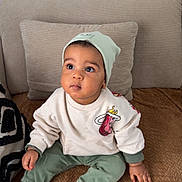 Kassim participe au concours pour gagner de l'argent avec cette photo : baby, child, beanie, sweatshirt, green_pants, socks, couch, pillow, indoors, cute, portrait, seated, looking_up, cozy, casual_clothing, infant, comfortable, home, soft_furniture, curious