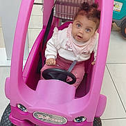 Talya a rejoint le concours — aidez-le/la à gagner de superbes lots ! toddler, child, toy_car, pink, indoor, floor_tiles, steering_wheel, curly_hair, clothing, sitting, play, cute, face, eyes, expression, vehicle, small_wheels, plastic, buckle, shopping_cart