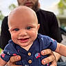 baby, child, smiling, person, hands, blue_eyes, shirt, buttons, flag_pattern, outdoor, blurred_background, adult, holding, happy, face, portrait, cute, infant, skin, casual_clothing