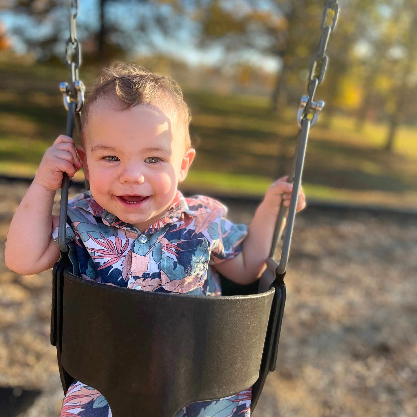 Christian Jr joined the competition — help win amazing prizes! blurred_background, child, curly_hair, daylight, fun, happy, joy, metal_chains, nature, outdoor, park, playground, seat, shirt, shorts, smiling, summer, sunlight, swing, toddler