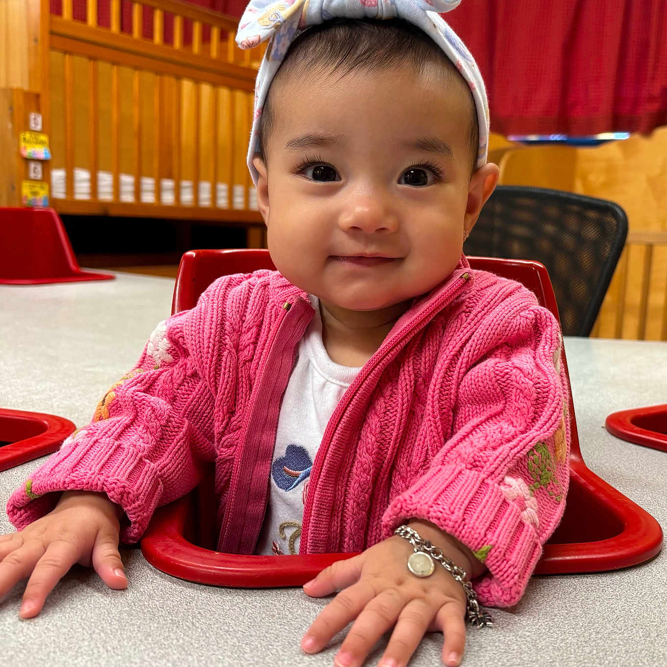 Arely joined the competition — help win amazing prizes! baby, bracelet, chair, child, cozy, crib, curtains, cute, face, hands, happy, headband, indoor, person, pink_sweater, portrait, smiling, table, toddler, wooden_furniture