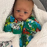 Xavier is registered to the contest to win money with this photo: baby, child, blanket, onesie, colorful_clothing, animal_print, tiger, leaves, infant, face, portrait, couch, fabric, soft_texture, indoor, young_child, curious_expression, wrapped, cozy, person
