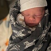 Hudson Bear is registered to the contest to win money with this photo: newborn, baby, sleeping, hat, blanket, swaddled, face, infant, cozy, soft_lighting, peaceful, closeup, cute, patterned_blanket, indoors, portrait, headwear, child, resting, warm