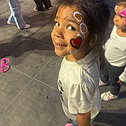 Athena joined the competition — help win amazing prizes! child, face_paint, heart, white_shirt, pink_shoes, curly_hair, outdoor, pavement, festival, event, smiling, standing, people, casual_clothing, young_girl, curious, daylight, crowd, fun, colorful