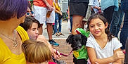 Levi joined the competition — help win amazing prizes! adult, bracelet, casual_clothing, child, costume, crowd, dinosaur_costume, dog, face, hair, leash, outdoor, pavement, people, shoes, shorts, sitting, smiling, street, tshirt