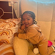 River is registered to the contest to win money with this photo: toddler, child, smiling, braided_hair, beads, hoodie, sweatpants, sneakers, couch, pillow, rainbow_pattern, indoor, cozy, happy, playful, person, furniture, home, cute, portrait