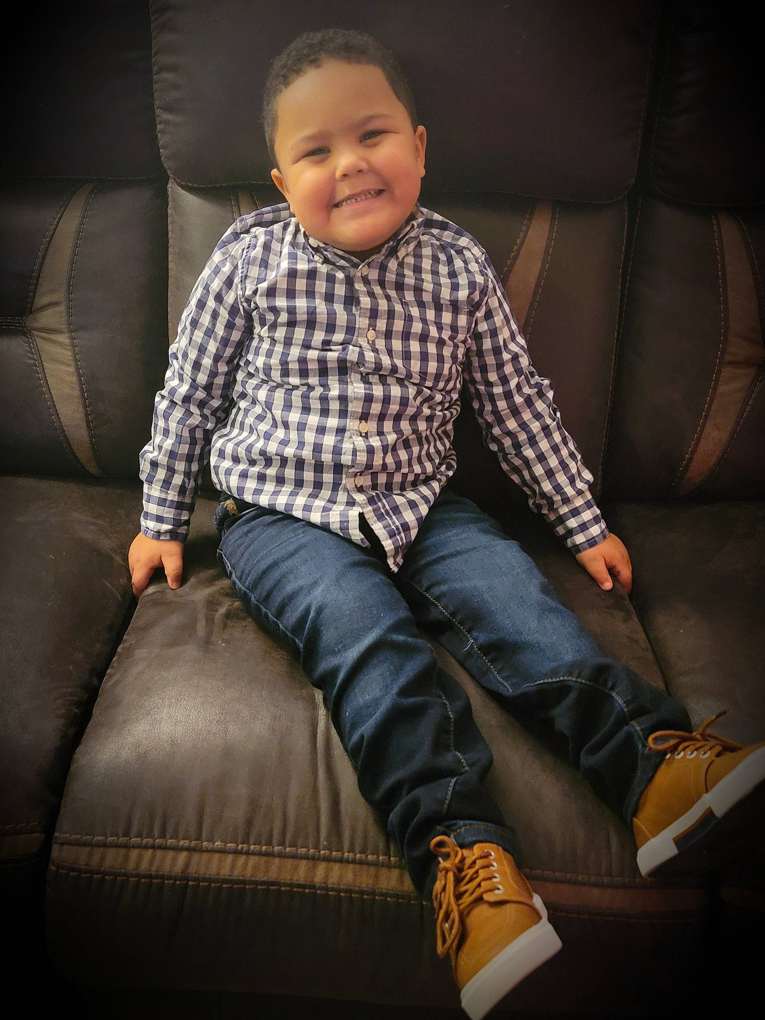 Tayvon is registered to the contest to win money with this photo: baby_toddler_clothing, collar, comfort, couch, denim, dress_shirt, face, flash_photography, head, human_leg, joy, knee, leg, lighting, pattern, person, plaid, sleeve, smile, textile