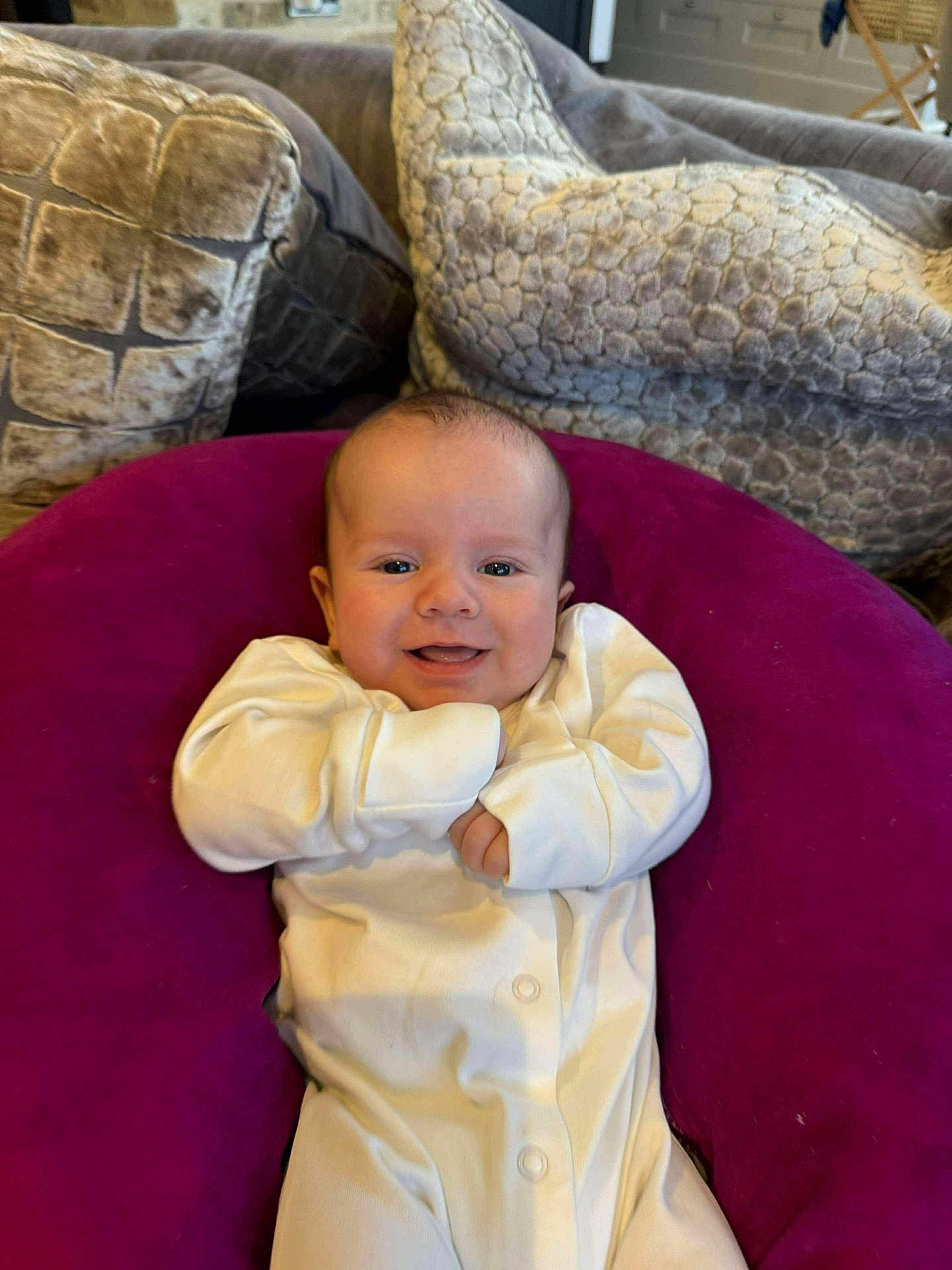Rowan joined the competition — help win amazing prizes! baby, smiling, onesie, purple_cushion, couch, pillows, indoor, face, child, happy, infant, cozy, homedecor, comfort, person, cute, relaxing, small_child, seated, soft_furniture
