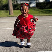 Nyomi joined the competition — help win amazing prizes! child, girl, red_dress, plaid_skirt, outdoor, laughing, smiling, sunny, pavement, shadow, black_shoes, white_socks, hair_bows, braids, necklace, earrings, greenery, tree, daylight, happy