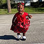 child, girl, red_dress, plaid_skirt, outdoor, laughing, smiling, sunny, pavement, shadow, black_shoes, white_socks, hair_bows, braids, necklace, earrings, greenery, tree, daylight, happy