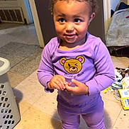Amariana is registered to the contest to win money with this photo: toddler, child, purple_outfit, indoor, floor, socks, cartoon_character, smile, standing, laundry_basket, messy_floor, curly_hair, person, cute, playful, home, clothing, expression, young, casual
