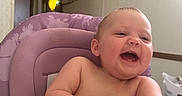 Lainey is registered to the contest to win money with this photo: baby, child, high_chair, laughing, smiling, indoor, furniture, purple, person, happy, arm, face, expression, skin, head, table, room, door, laundry_basket, home