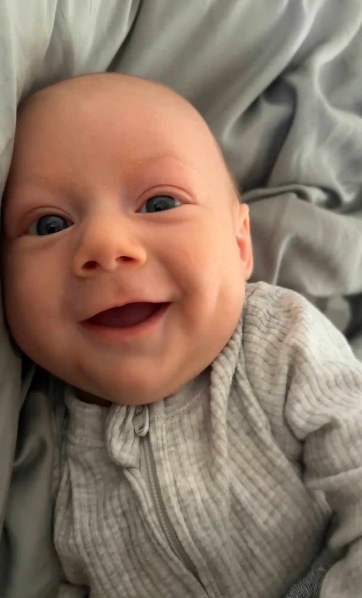 Jackson joined the competition — help win amazing prizes! baby, smiling, face, eyes, clothing, ribbed_fabric, zipper, infant, cozy, blanket, bed, happy, cute, closeup, skin, person, young_child, indoors, soft_texture, portrait
