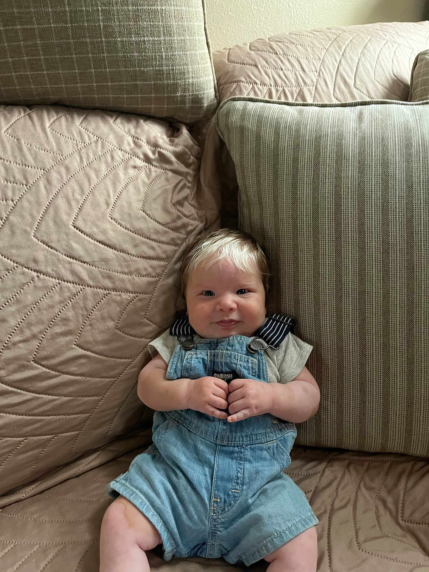 Thiago is registered to the contest to win money with this photo: baby, infant, smile, overalls, denim, couch, cushion, indoor, child, cute, comfortable, striped_shirt, plush, soft_lighting, happy, portrait, seated, young_child, homedecor, relaxed