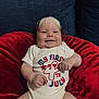 baby, infant, smile, red_cushion, blue_sofa, onesie, clothing, sitting, happy, face, skin, arm, hand, leg, indoor, celebration, holiday, cute, child, portrait