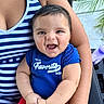 Samuel is registered to the contest to win money with this photo: baby, child, smiling, happy, person, face, clothing, blue_shirt, red_pants, striped_tank_top, arm, hand, outdoor, plant, chair, bottle, portrait, closeup, sitting, infant