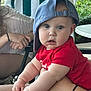 baby, child, cap, red_shirt, blue_cap, curious_expression, chubby_arms, adult_hand, outdoor, greenery, towel, seated, person, casual, skin, table, chair, daylight, portrait, hands