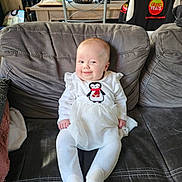 Kélya a rejoint le concours — aidez-le/la à gagner de superbes lots ! baby, child, smiling, couch, indoor, white_clothing, penguin_design, seat, furniture, home, cozy, person, infant, cute, happy, portrait, sitting, soft_toys, blanket, room