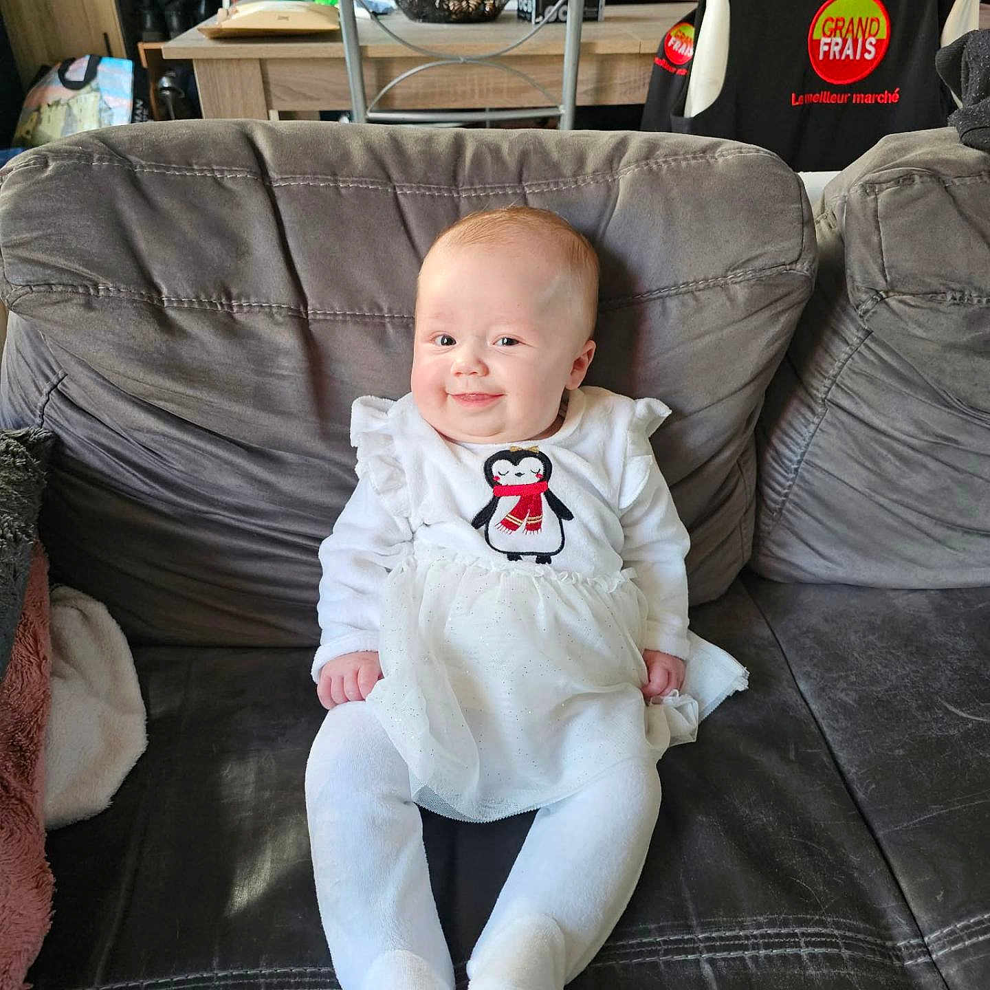 Kélya a rejoint le concours — aidez-le/la à gagner de superbes lots ! baby, child, smiling, couch, indoor, white_clothing, penguin_design, seat, furniture, home, cozy, person, infant, cute, happy, portrait, sitting, soft_toys, blanket, room