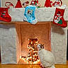cat, fireplace, christmas_stockings, holiday_decorations, fairy_lights, indoor, festive, decor, white_cat, orange_cat, floor, mantel, stockings, lights, cozy, curious_cat, winter, celebration, home, seasonal