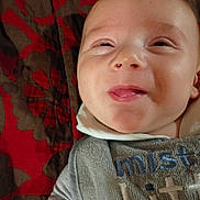 Ja'Riah is registered to the contest to win money with this photo: baby, child, face, smile, tongue_out, bib, clothing, blanket, pattern, red, brown, happy, infant, portrait, cute, young, person, lying_down, close_up, skin