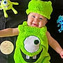 baby, child, costume, halloween, green, plush_toy, smile, face, hat, monster, cute, happy, infant, black_background, soft_texture, teeth, eye, celebration, holiday, lying_down