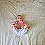 Irina participe au concours pour gagner de l'argent avec cette photo : baby, infant, smiling, lying_down, pink_shirt, white_pants, patterned_bedspread, wooden_sign, feet_up, cute, child, person, indoors, bed, fabric, happy, young, portrait, human, sleepwear
