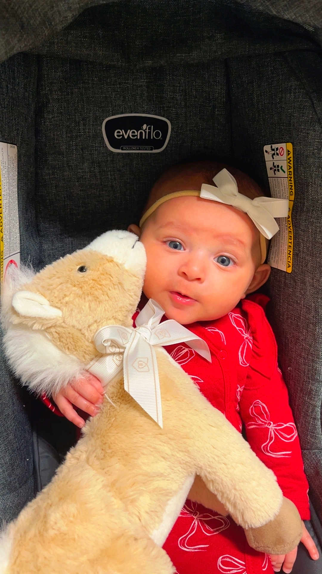 Abria joined the competition — help win amazing prizes! baby, child, stuffed_animal, car_seat, red_clothing, headband, bow, plush_toy, cute, infant, portrait, indoor, person, soft_toy, blue_eyes, cuddling, comfort, smiling, closeup, seat