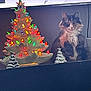 cat, calico_cat, ceramic_tree, christmas_tree, holiday_decor, lights, multicolored_lights, silver_tree, figurine, decor, indoor, fluffy, pet, feline, animal, sitting, dark_background, closed_sign, festive, ornament