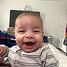 Thiago joined the competition — help win amazing prizes! baby, child, smiling, laughing, striped_clothing, indoor, bed, laundry_basket, television, happy, person, face, head, hair, onesie, furniture, blanket, door, room, casual