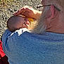 baby, newborn, elderly_man, beard, glasses, outdoor, sunlight, grass, rocky_ground, holding, cradling, peaceful, sleeping, tenderness, affection, person, close_up, portrait, gray_hair, casual_clothing