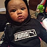 baby, background, carpet, casual, child, close_up, cute, dark_clothing, expression, eyes, face, hoodie, indoor, infant, lips, portrait, puma_logo, sitting, sweatshirt, toy