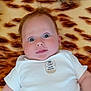 baby, infant, child, onesie, blanket, tiger_pattern, face, eyes, cute, expression, lying_down, soft_texture, animal_emblem, indoors, skin, head, young_child, portrait, warm_colors, curious