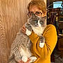 animal, blue_eyes, casual, cat, cozy, feline, fluffy_cat, glasses, gray_cat, holding, indoor, mustard_sweater, person, pet, portrait, reflection, warm_colors, white_paws, window, wooden_wall