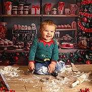 Timaë participe au concours pour gagner de l'argent avec cette photo : toddler, child, smiling, flour, cookie_cutters, rolling_pin, cookbook, wooden_table, christmas_tree, holiday_decorations, baking, kitchen, festive_clothing, candle, eggs, jar, cup, background, indoors, happy