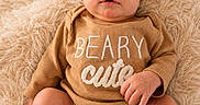 Julian is registered to the contest to win money with this photo: baby, infant, onesie, brown_clothing, text_on_clothing, fluffy_blanket, soft_texture, cute, portrait, sitting, barefoot, skin, face, eyes, hands, feet, newborn, cozy, indoor, child