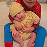 Julian is registered to the contest to win money with this photo: child, baby, pajamas, bed, pillow, indoor, siblings, smiling, holding, yellow_outfit, hat, barefoot, happy, family, cozy, cute, portrait, love, tender, casual