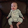 baby, infant, smiling, pajamas, animal_prints, leather_couch, sitting, happy, child, indoors, cute, comfortable, portrait, person, young_child, one_person, small_child, clothing, relaxing, home