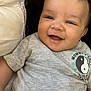 baby, child, smile, face, eyes, shirt, grey_clothing, yin_yang, cushion, pillow, happy, infant, person, portrait, cute, indoors, skin, head, young_child, closeup