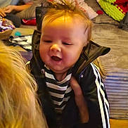 Demonta is registered to the contest to win money with this photo: baby, black_jacket, blurred_background, casual_clothing, child, couch, furniture, hair, hand, happy, home, indoor, living_room, person, pillow, seated_person, smile, soft_lighting, striped_clothing, young_child