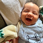 Demonta is registered to the contest to win money with this photo: baby, smiling, infant, blanket, pillow, clothing, cute, face, happy, portrait, child, indoors, cozy, soft, relaxed, lying_down, cute_outfit, button, dog_print, skin