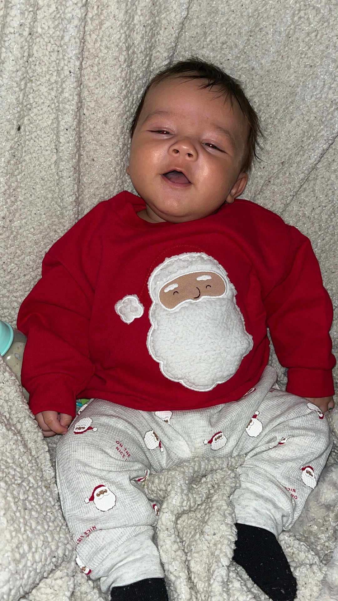 Demonta is registered to the contest to win money with this photo: baby, infant, child, pajamas, santa_claus, red_sweater, patterned_pants, blanket, cozy, smiling, happy, indoors, cute, holiday, christmas, warm, soft_texture, face, person, sitting