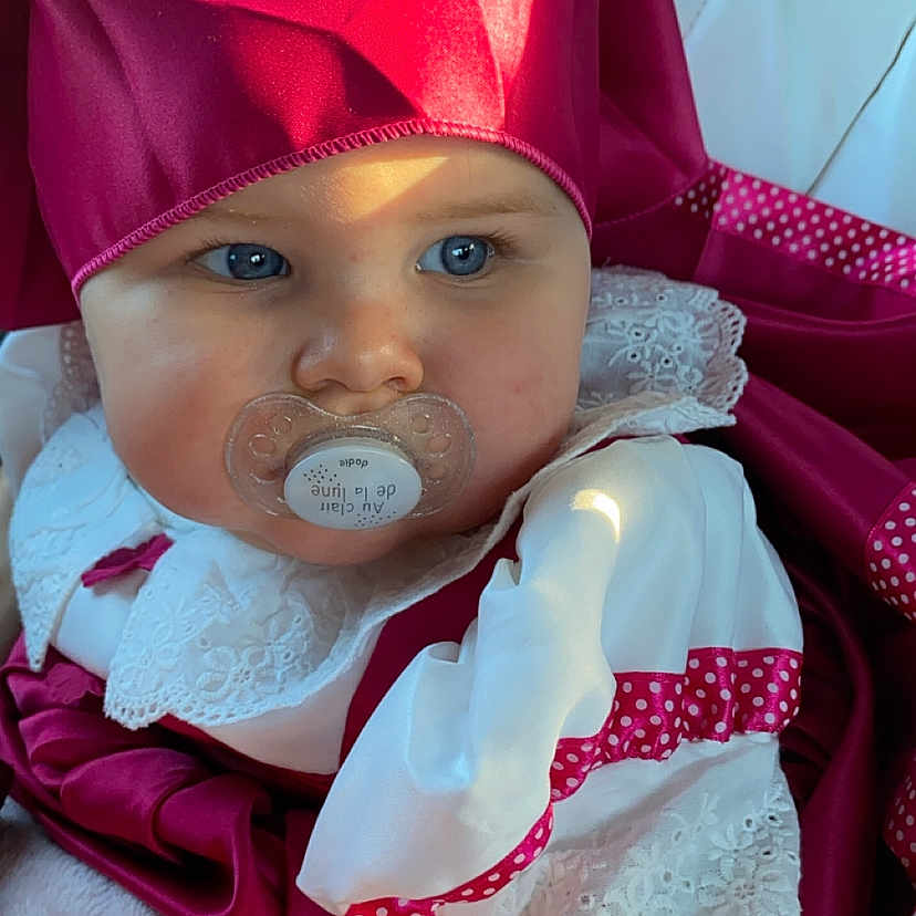 Alba a rejoint le concours — aidez-le/la à gagner de superbes lots ! adorable, baby, baby_clothes, blue_eyes, bonnet, child, closeup, cute, expression, face, indoor, infant, lace, magenta_clothing, pacifier, portrait, sitting, soft_light, white_clothing, young_child