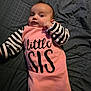 Zoey is registered to the contest to win money with this photo: baby, infant, child, person, pink_clothing, striped_sleeves, text_on_clothing, laying_down, blanket, quilt, portrait, cute, face, expression, young, sleepwear, indoor, cozy, soft_light, casual